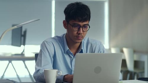 Young professional business male using computer looking information paper at office.