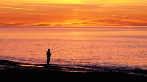 Silhouette eines Fischers mit einer Angelrute bei Sonnenuntergang über dem Meer