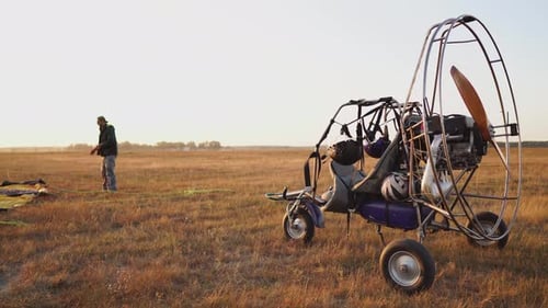 The Motor Paraglider Stands in the Field at Sunset with a Wooden Propeller, and the Pilot Lays Out