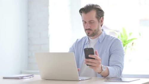 Man Working on Laptop and Using Phone