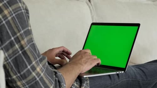 Close-up of a Man Uses Laptop with Green Mock-up Screen While Sitting on sofa in His Cozy Living