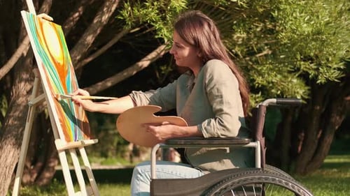 A Disabled Woman in a Wheelchair Paints a Picture in the Park in Sunny Summer Weather