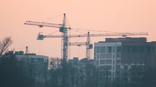 Dark Silhouette of Tower Cranes at High Residential Apartment Buildings Construction Site at Sunset