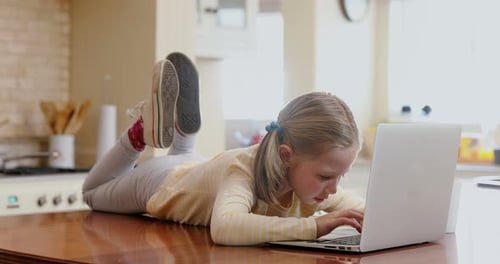 Happy little girl lying on table using her laptop 4K 4k