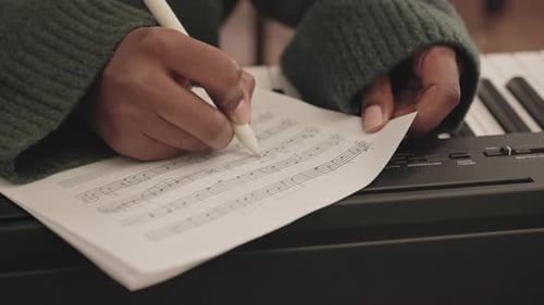 Hands Writing Music on Sheet Over Keyboard