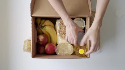 Une femme sort des produits alimentaires de la boîte à dons, vue de dessus