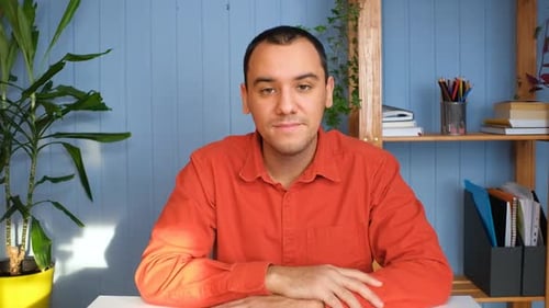 Young Man Sits at Desk Looking into Camera