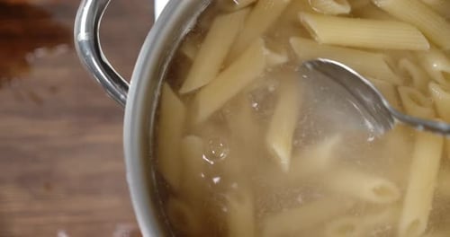 Boiled Penne Pasta Stirred with a Spoon in the Pot.
