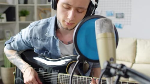 Young Adult Playing Guitar and Singing into Microphone