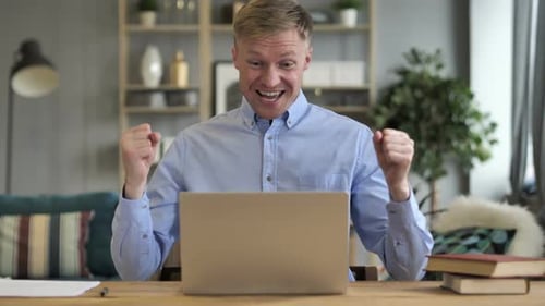 Man Celebrates Success at Laptop in Home Office