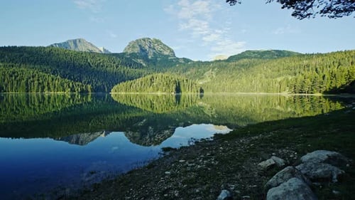 Walking Along a Lake Shore at Sunrise with a View To Distant Mountain Peaks and Forested Foothills