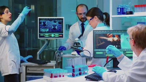 Senior Chemist Analysing Blood Sample While Coworkers Discussing