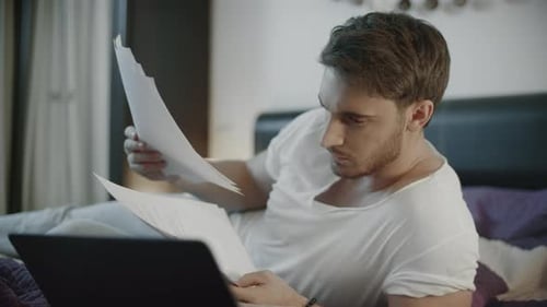 Man Reviews Documents While Reclining on Bed