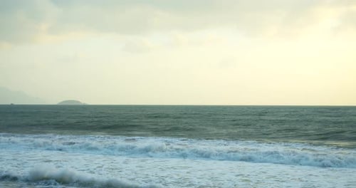 A Large Sun Appears From Behind the Clouds and Large Mountains Touch the Horizon and Coast