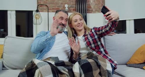 Pareja relajándose en un suave sofá doméstico por la noche y haciendo una selfie
