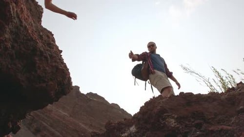 Man Helping Woman Jump Over Red Clay Hill