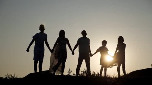 Siluetas de una familia levantando las manos en la colina bajo un cielo despejado