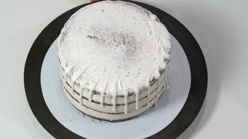 Top View of a Baker Pouring Melted White Chocolate on the Edges of the Cake so It Drips Down the