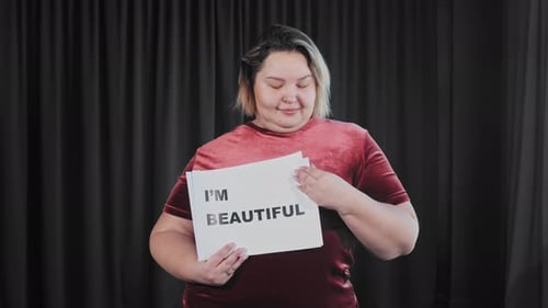 Une femme en surpoids confiante et affectueuse tenant une plaque signalétique avec un signe « Je suis belle et je m'aime »