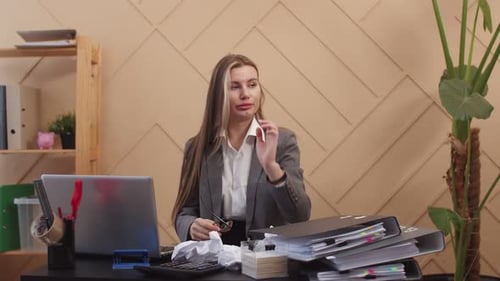 Office Worker Woman Tiredly Straightens Hair and Puts Head on Hand While Sitting at Table with