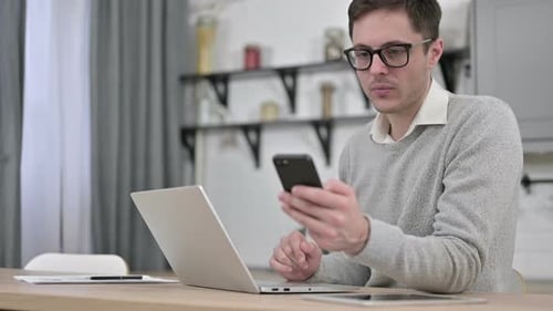 Man Uses Laptop and Smartphone at Desk