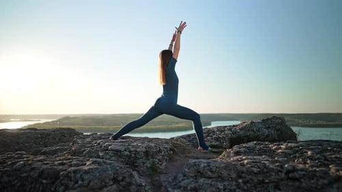 Sporty Woman in Blue Costume Practicing Yoga on High Rock Above Water