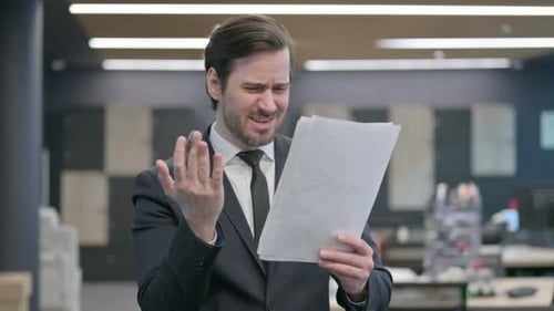 Frustrated Man Reviews Documents in Office
