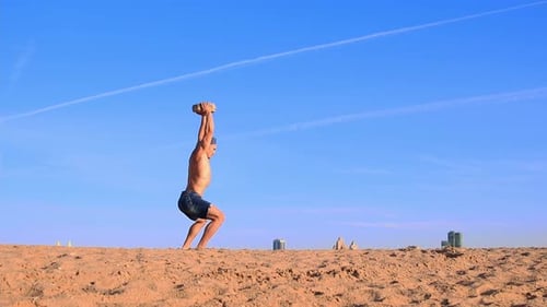 Young Fit Man Doing Sports Exercises at the Beach Holding a Heavy Rock in His Hands