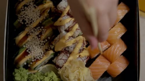 Top View of Hand Picking Up Sushi Rolls From Trays Full of Sushi