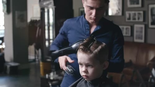 Stylist Brushes and Dries Child's Hair at Barbershop