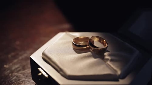 Two Gold Matrimony Wedding Rings Lying on White Gift Box Shining with Warm Light Close Up Macro