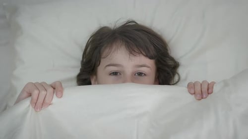 Frightened Child Hiding Under White Bed Sheets