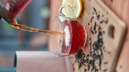VERTICAL VIDEO POV Gießen Sie schwarzen heißen Tee mit frischem Duft von der Teekanne bis zur transparenten Glasschale