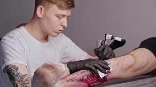 Young Ginger Man Filling the Tattoo on the Leg of His Client