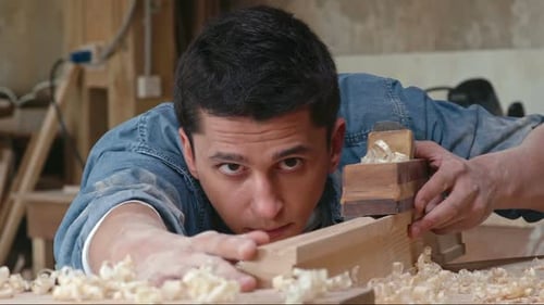 Young Craftsman Planes Wood in Workshop