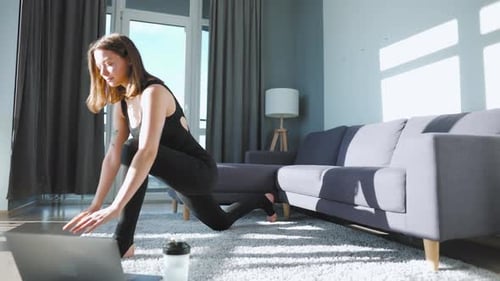 Joven mujer caucásica con un mono negro haciendo yoga en casa para desarrollar la flexibilidad y el equilibrio en el