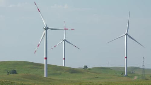 Motion the Blades of a Large Wind Turbine in a Field Against a Background of Cloudy Blue Sky with