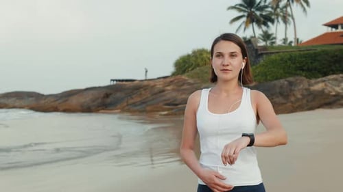 Athletic Woman Runs on Tropical Beach with Smartwatch