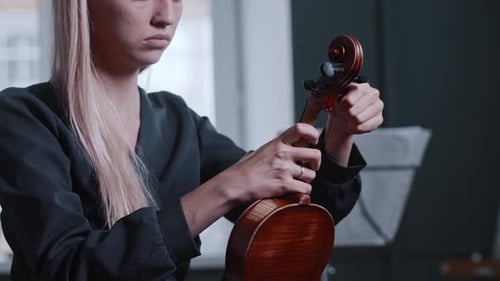 Young Woman Adjusting Violin Strings Before Playing