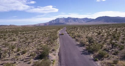 Aerial view of yellow sport car driving on asphalt road in the middle of dusty dry desert land.