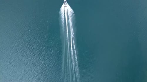 Aerial follow top down view of person wakeboarding on a lake early in the morning.