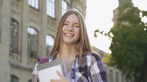 Retrato de estudante feliz e sorridente em pé perto do prédio da faculdade
