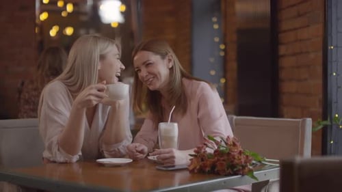 Fröhliche Mutter und ihre erwachsene Tochter chatten bei Kaffee