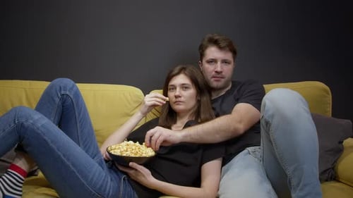 Couple Eating Popcorn Together on Couch at Home