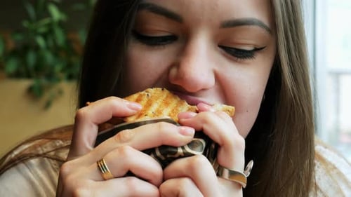 Young Hungry Woman Eats Toast in a Cafe, Fast Food Restaurant