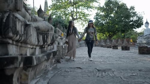 Two Thai Girls Travel Inside Wat Yai Chai Mongkhon Temple in Ayutthaya at Sunset Walking Along a Row