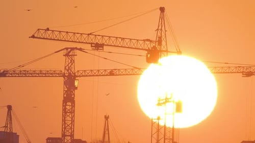 Dark Silhouette of Tower Cranes with Big Setting Sun at High Residential Apartment Buildings