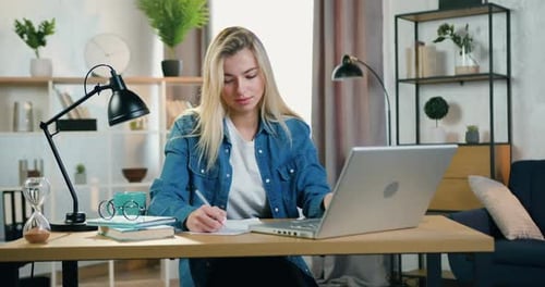 Jeune femme blonde travaillant avec un ordinateur portable et transformant les notes nécessaires en documents au bureau à domicile