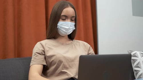 Young Adult Works on Laptop Wearing Mask Indoors