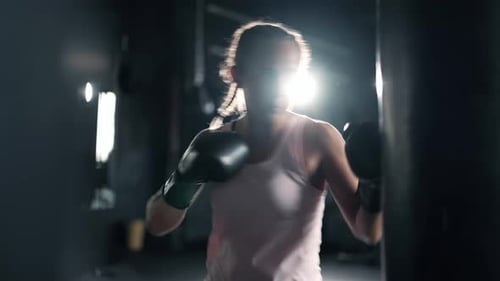A Muscular Alone Woman is Hits Punching Bag in the Gym